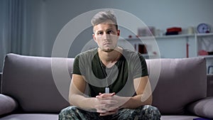 Sad male military sitting on sofa and looking at camera, psychological trauma