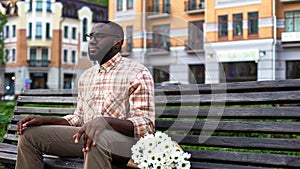 Sad male nervously waiting for girl, sitting park bench with flowers, blind date