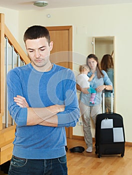 Sad man against wife with baby and suitcase