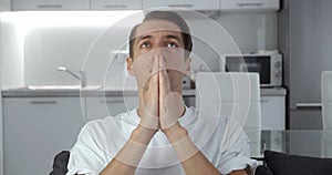 Sad man asking for help about problem, praying to God. Religious male sit on sofa at home put hands in prayer. Guy