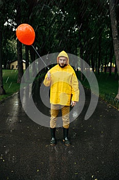 Sad man with balloon walking in park in rainy day