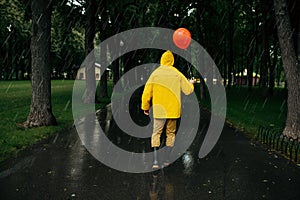 Sad man with balloon walking in park in rainy day