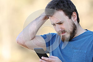 Sad man checking smart phone bad content outdoors