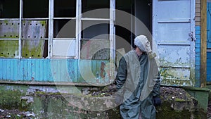 Sad man with a gas mask sits amid the ruined house