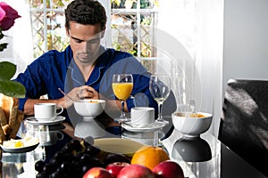 Sad man in his pijamas, sitting at breakfast table with one empty place and chair