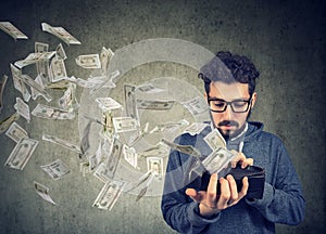 Hipster man looking at his wallet with money dollar banknotes flying out away photo