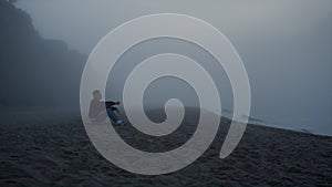 Sad man looking sea landscape in fog. Serious guy sitting on sandy beach