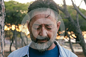 Sad man portrait expression face close up in outdoor park. One adult mature male people with closed eyes looking down. Problems on