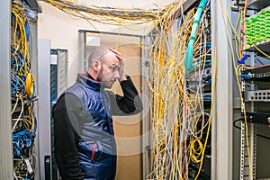 A sad man put his hand to his face at the sight of problems with laying wires in the server room. Incorrect connection of