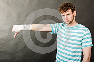 Sad man showing thumb down by bandaged hand.