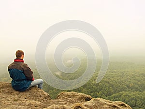 Sad man sit on the peak of sandstone rock and watching over the misty and foggy morning valley.