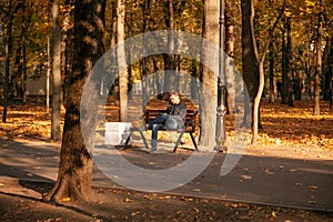Sad man is sitting on a bench in an autumn city park with bouquet of flowers and waits for a long time. A failed date