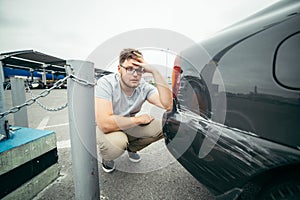 Sad man standing near car with scratch