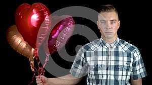 A sad man stands with helium balls on a black background. Valentine`s Day is the day of all lovers.