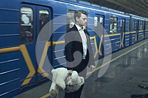 Sad man with a teddy bear in a subway.