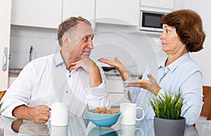 Sad mature couple discussing, quarrel at home kitchen indoor