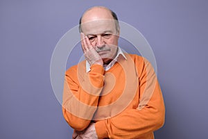 Sad mature hispanic man in orange sweater feeling stressed and alone