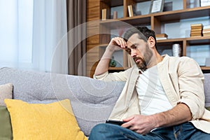 Sad mature man in depression sitting alone at home on sofa in living room