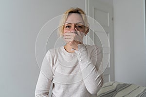 Sad mature woman closes mouth with hand.