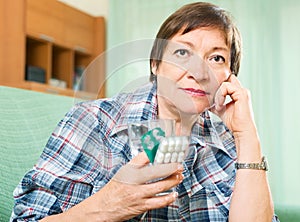 Sad mature woman with pills and glass of water