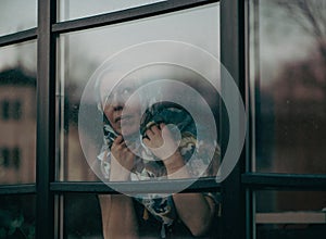 middle-aged woman with scarf on head looking through the dirty window glass photo