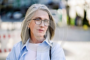 Sad mature woman with silver hair and glasses in a European city, portraying feelings of loneliness, depression, and