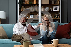 Sad mature woman sitting away from her husband after having quarrel. Senior couple not talking having argue at their home.