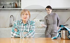 Sad mature woman with soup in pan on table listens unpleasant sayings of adult daughter. photo