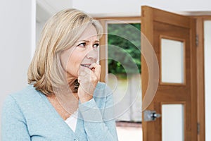Sad Mature Woman Suffering From Agoraphobia Looking Out Of Open photo