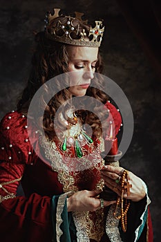 sad medieval queen in red dress with candle and crown