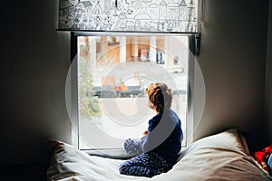 Sad and melancholic boy looks through a window in his apartment during his confinement