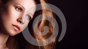 Sad, melancholy girl with long red hair on a dark background photo