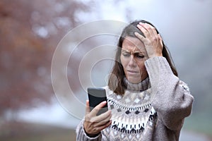 Sad middle age woman checking phone in autumn