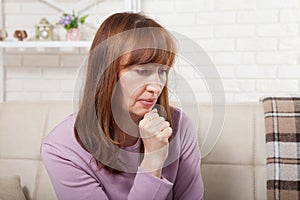 Sad middle age woman sitting on a sofa in the living room. Menopause