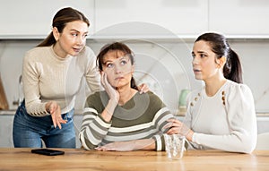 Sad middle-aged woman sitting at table while two others trying to calm her