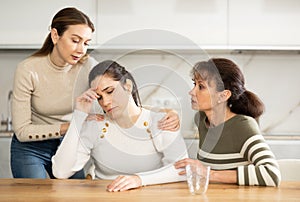 Sad middle-aged woman sitting at table while two others trying to calm her