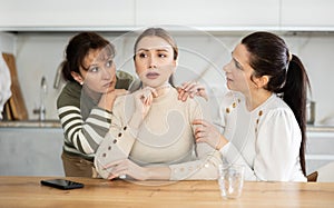 Sad middle-aged woman sitting at table while two others trying to calm her
