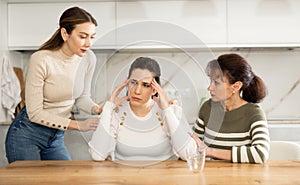 Sad middle-aged woman sitting at table while two others trying to calm her