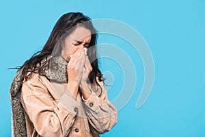 Sad millennial caucasian woman brunette patient with scarf blowing her nose, isolated on blue background