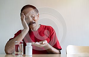 Sad mood. Portrait picture of an upset elderly Asian man sitting at a table and holding a weekly organizer