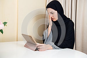 Sad Muslim busy business woman holding a tablet at home or office