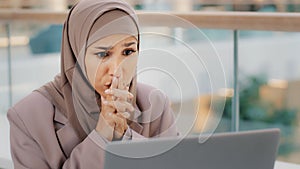 Sad muslim girl student in hijab looking at laptop screen reading email shocked by bad news frustrated businesswoman