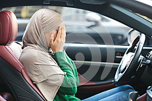 Sad muslim woman driving her car, crying, covering face