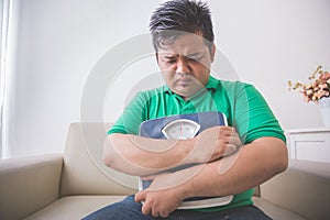 Sad obese man holding a weight scale, thinking about his weight