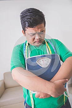 Sad obese man holding a weight scale, thinking about his weight