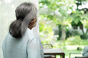 A sad old elderly woman uses Walker for standing in front of windows and looking outside and feeling lonely. Concept of depression