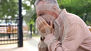 Sad old man sitting on hospital garden bench, pensioner crying in sorrow, loss