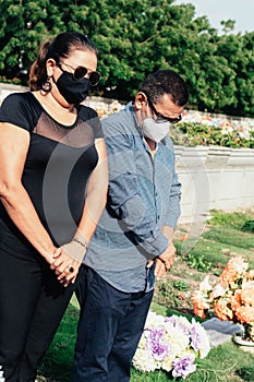 Sad older couple with protective mask at cemetery visiting a relative commemorating their ancestors