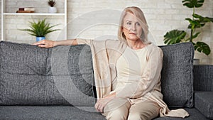 Sad older woman is sitting on a sofa at home