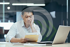 Sad over thinking asian businessman reading bad news letter from bank